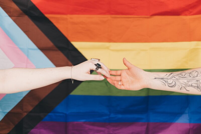 Hands Joined in front of Progress Pride Flag
