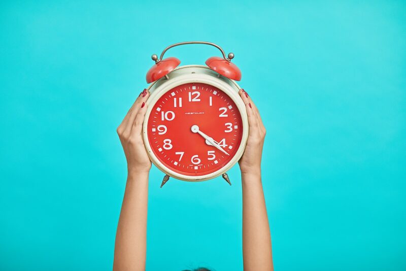 hands holding red analog alarm clock