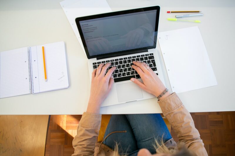 hands of woman working on laptop with notebook nearby