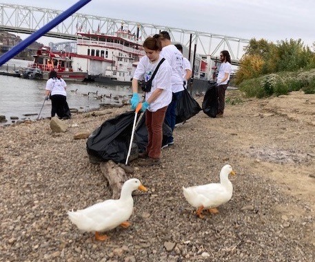 Students cleaning up debris while two ducks walk past them