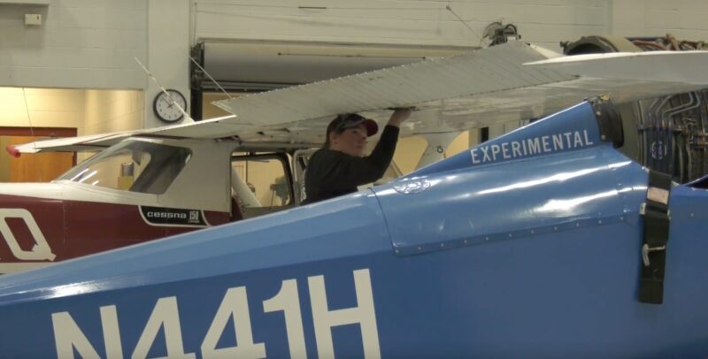 Screenshot of a female Aviation Maintenance Technology student working on a blue aircraft at Harrison Campus