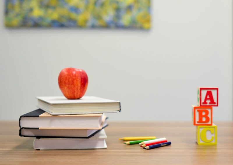 red apple on top of a stack of books on a table with pencils and 