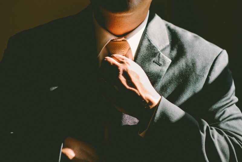 chin, shoulders, and hand of a man in a grey suit, straightening his tie