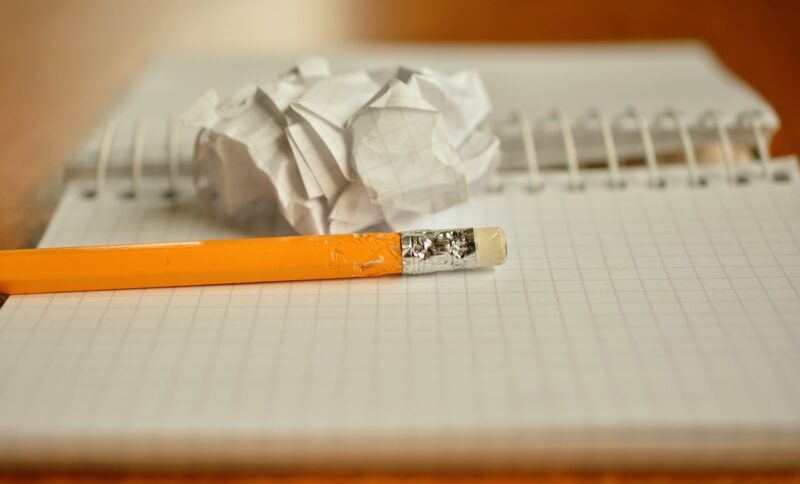 A pencil and a crumpled piece of paper on top of blank pages of an open notebook