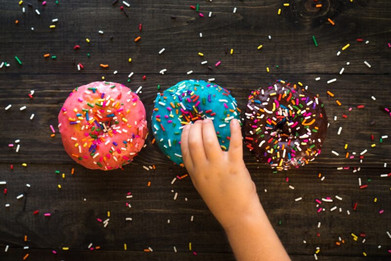 Three donuts on a black table with a hand reaching for the center donut