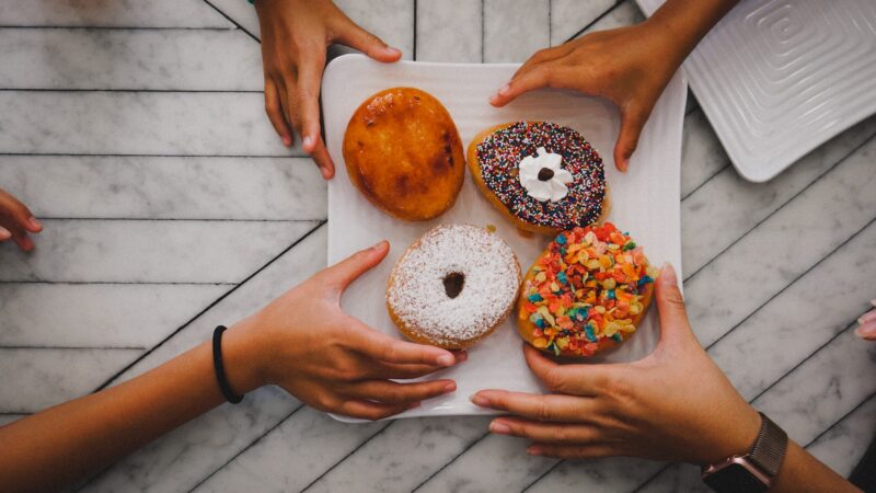 four hands reaching for four donuts on a plate