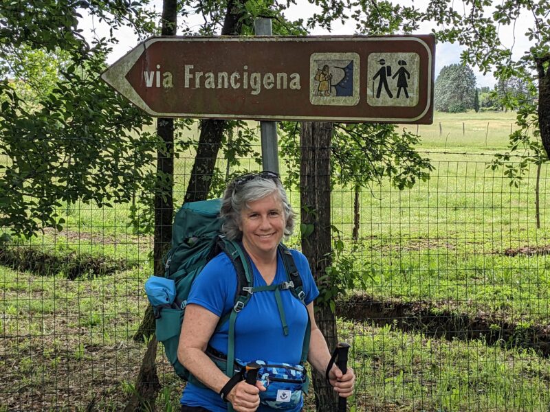 Karen Groh in hiking gear in front of Via Francigena sign
