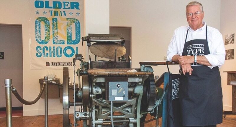 Gary Walton standing next to an antique printing press