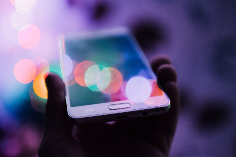 hand in shadow holding a cellphone with multicolored dots of light showing on the phone screen