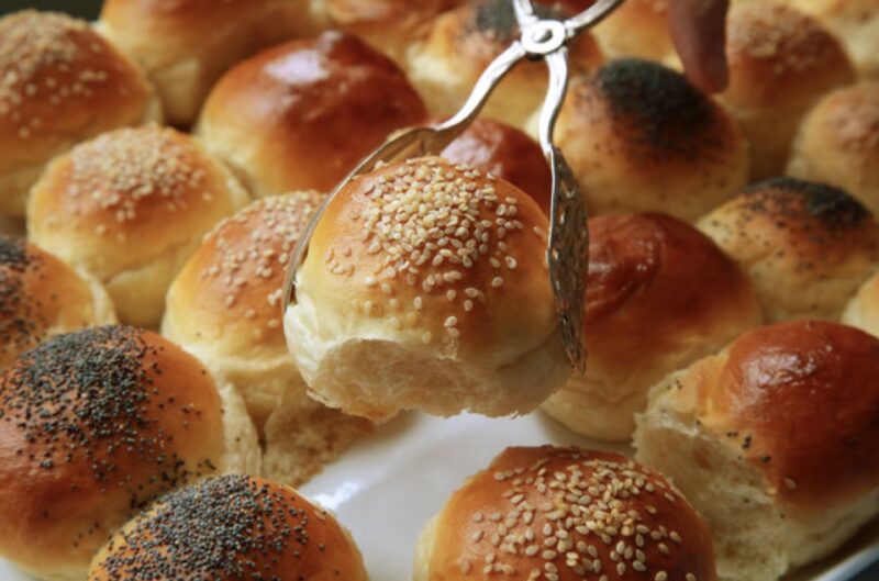 An assortment of dinner rolls with one roll being picked up with a pair of tongs