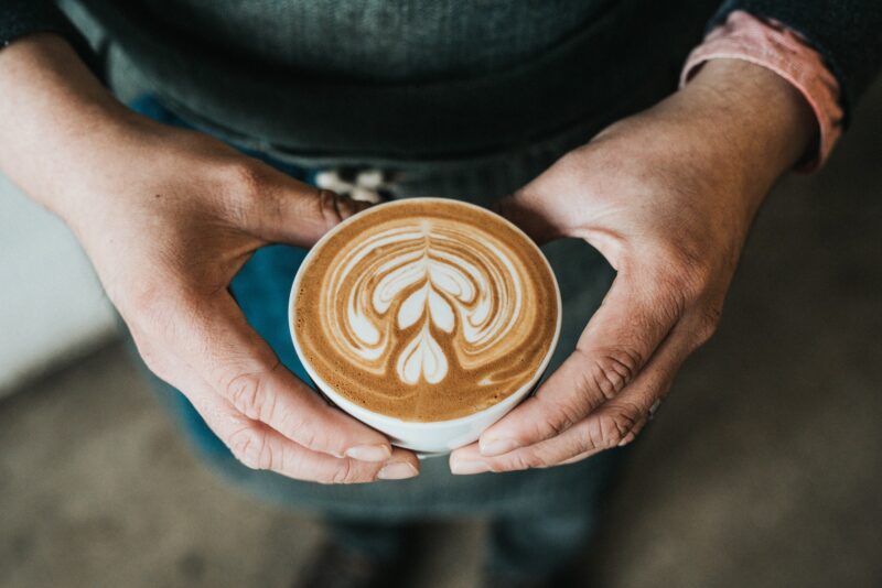 hands holding a coffee cup with a heart on the surface of the coffee