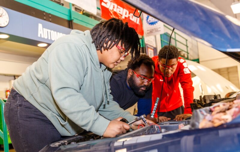 Three automotive students looking under the hood of a car