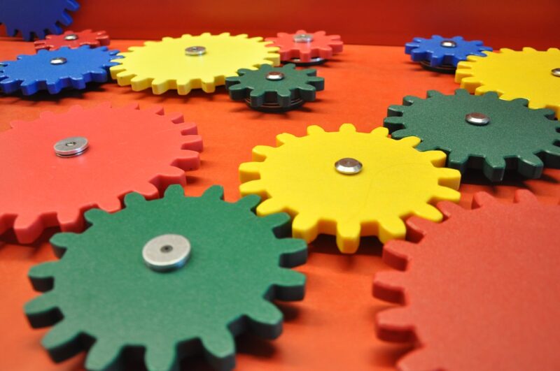 red, blue yellow, and green intersecting gears of various sizes on a red table