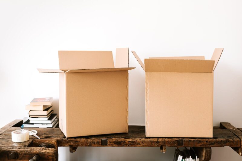 Two open cardboard boxes with a stack of books and packing tape on a wooden desk