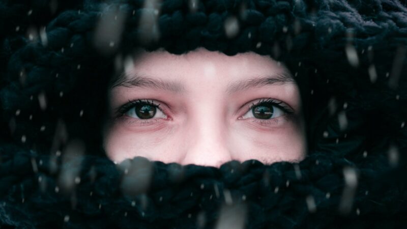 a woman's eyes and nose can be seen with a black fuzzy hood surrounding her face