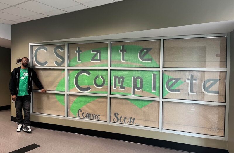 Jamal Lundy with the window sign he designed to announce the new CState Complete office in ATLC 201