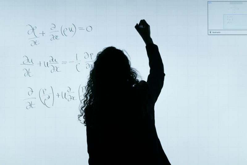 Back of a woman who is writing a math formula on a whiteboard