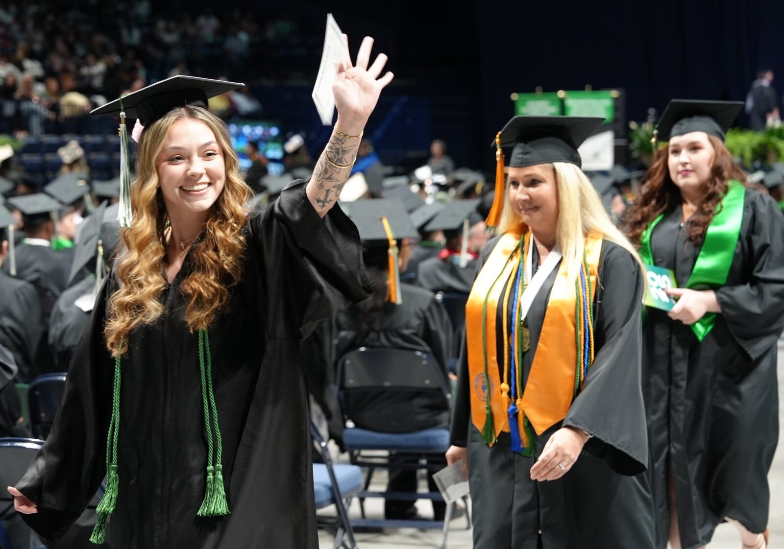 Two female graduates waving as they walk