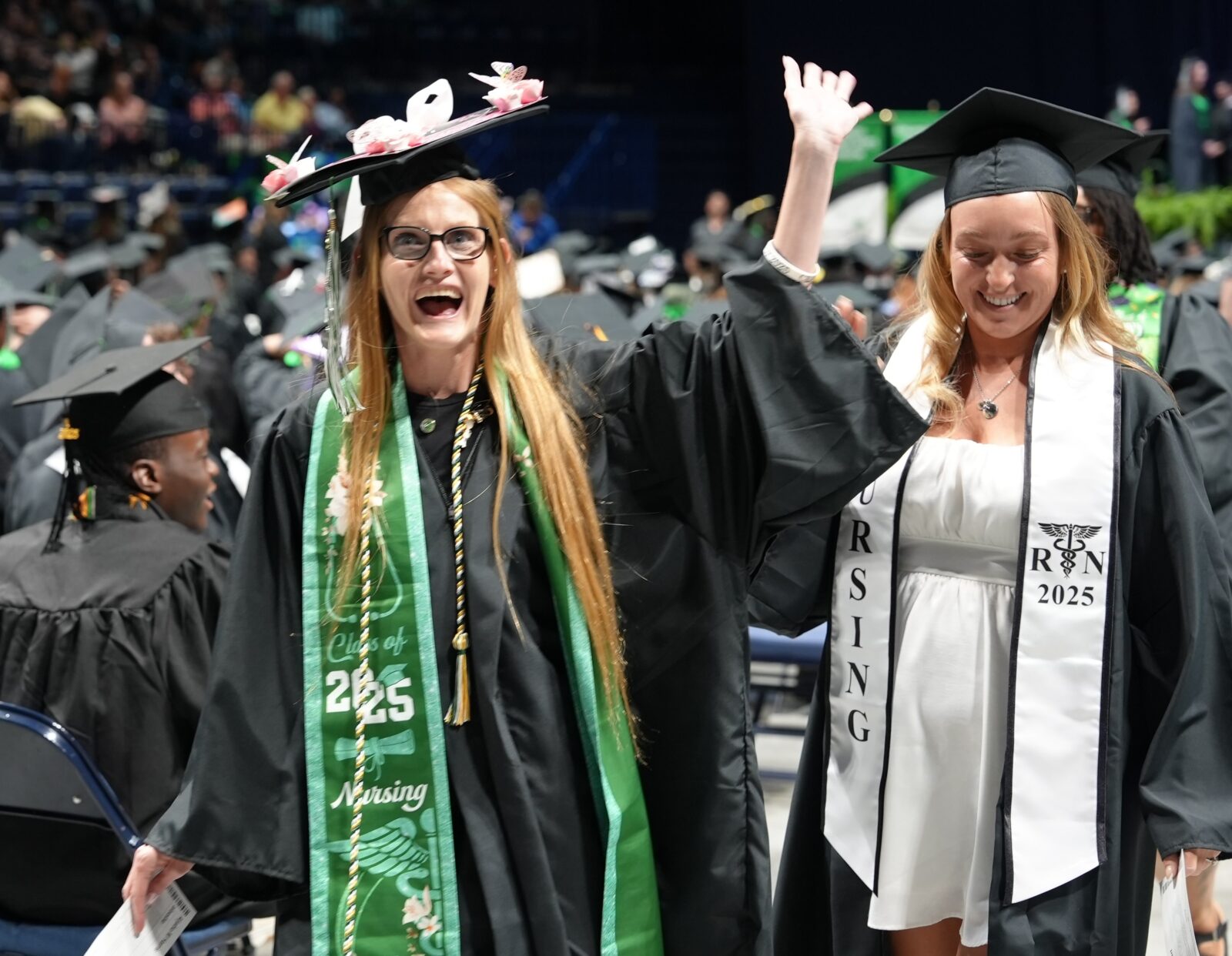 Two female graduates waving as they walk