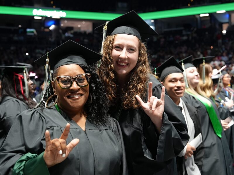 Two smiling female graduates making ASL