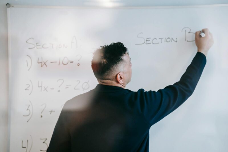 A male teacher writes equations on a whiteboard during a math lesson.