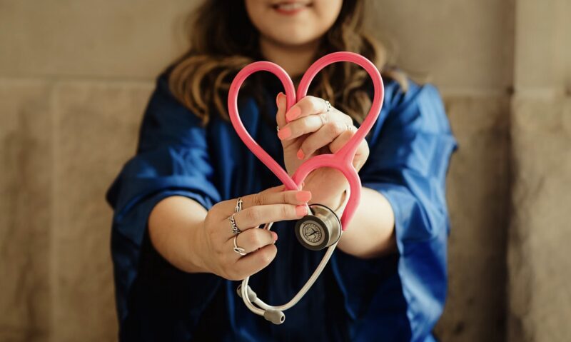 woman in blue scrubs holding a stethoscope with part of the cord in the shape of a pink heart